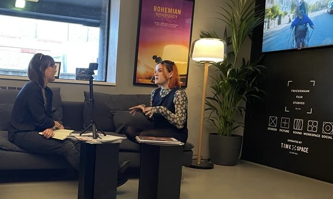 Two women are talking, sitting down on a sofa.