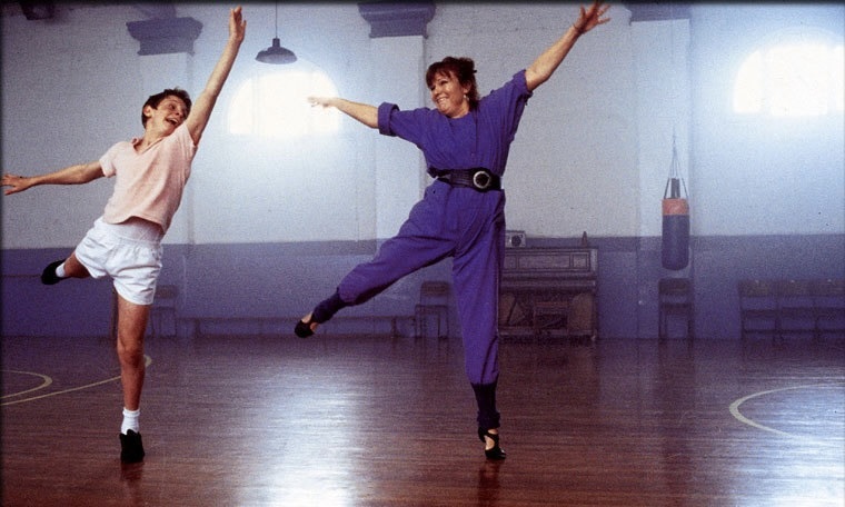 Billy and Mrs Wilkinson are dancing, arms lifted up in the air.