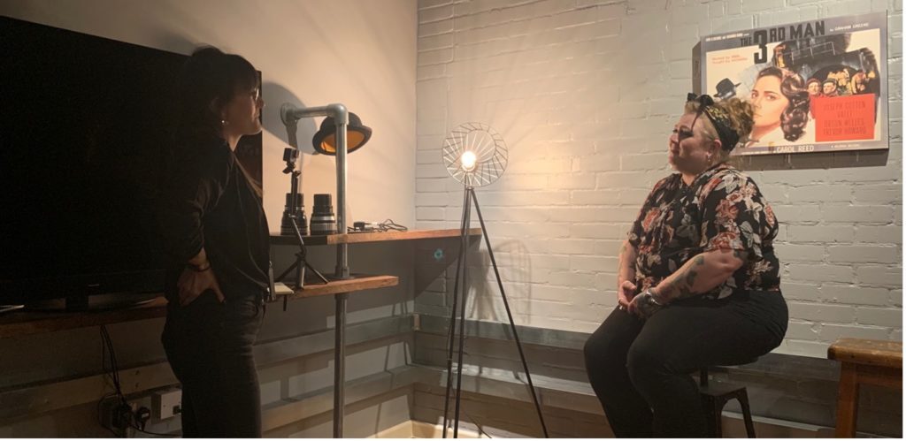 Two women are talking, one standing up while the other is sitting down.