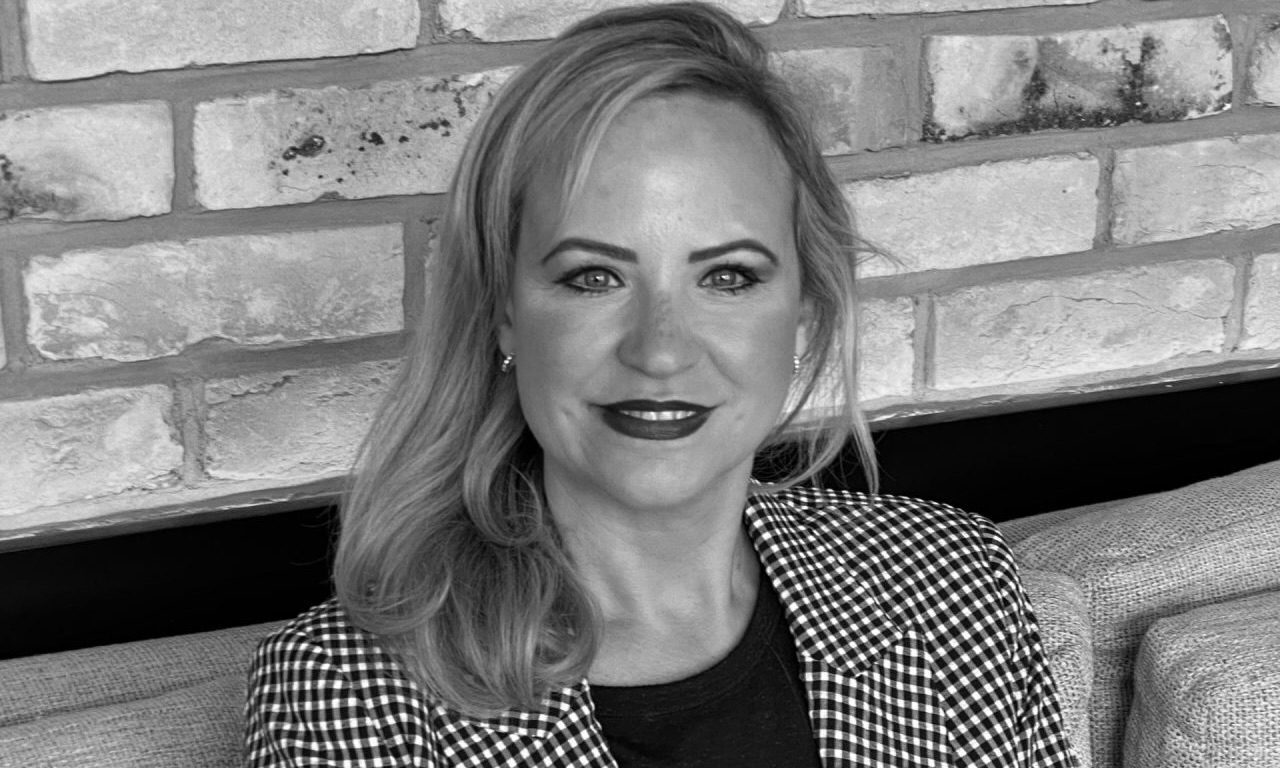 Sarah Dicks is smiling at the camera with a brick wall behind her.